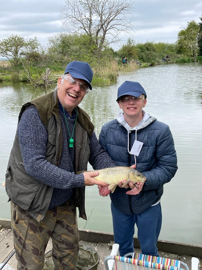 picture of a smiling caster and student both holding a fish from the lake. 