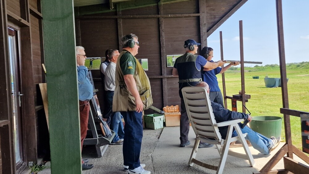 A picture taken from the shooting bay, with a young man having a go at shooting, with instructors looking on