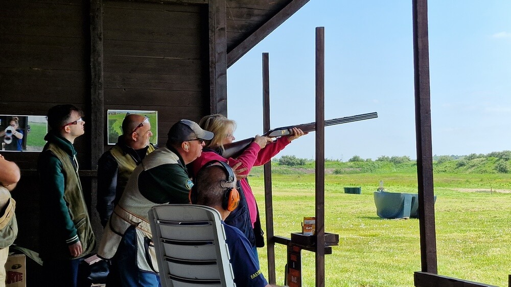 one of the ladies takes aim at a clay, with help and guidance from the shooting team. 