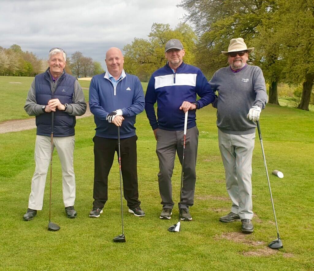 four of the golfers are ready on the first tee, standing holding the usual driver clubs.