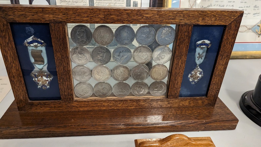 twenty silver crown pieces, each with the design on the reverse of St. George and the Dragon, the whole being mounted in a unique glass frame was presented to the Lodge.