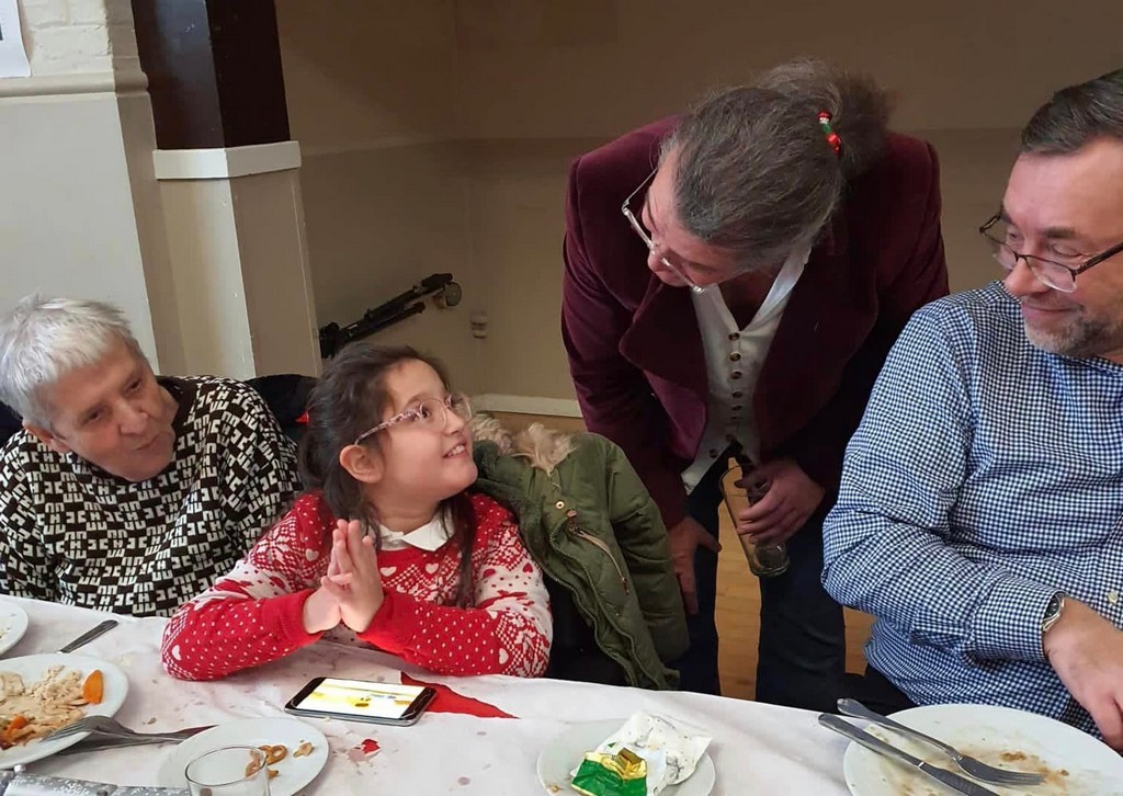 Mark Lawson speaking to a little girl enjoying her Christmas Lunch as the family look on. 